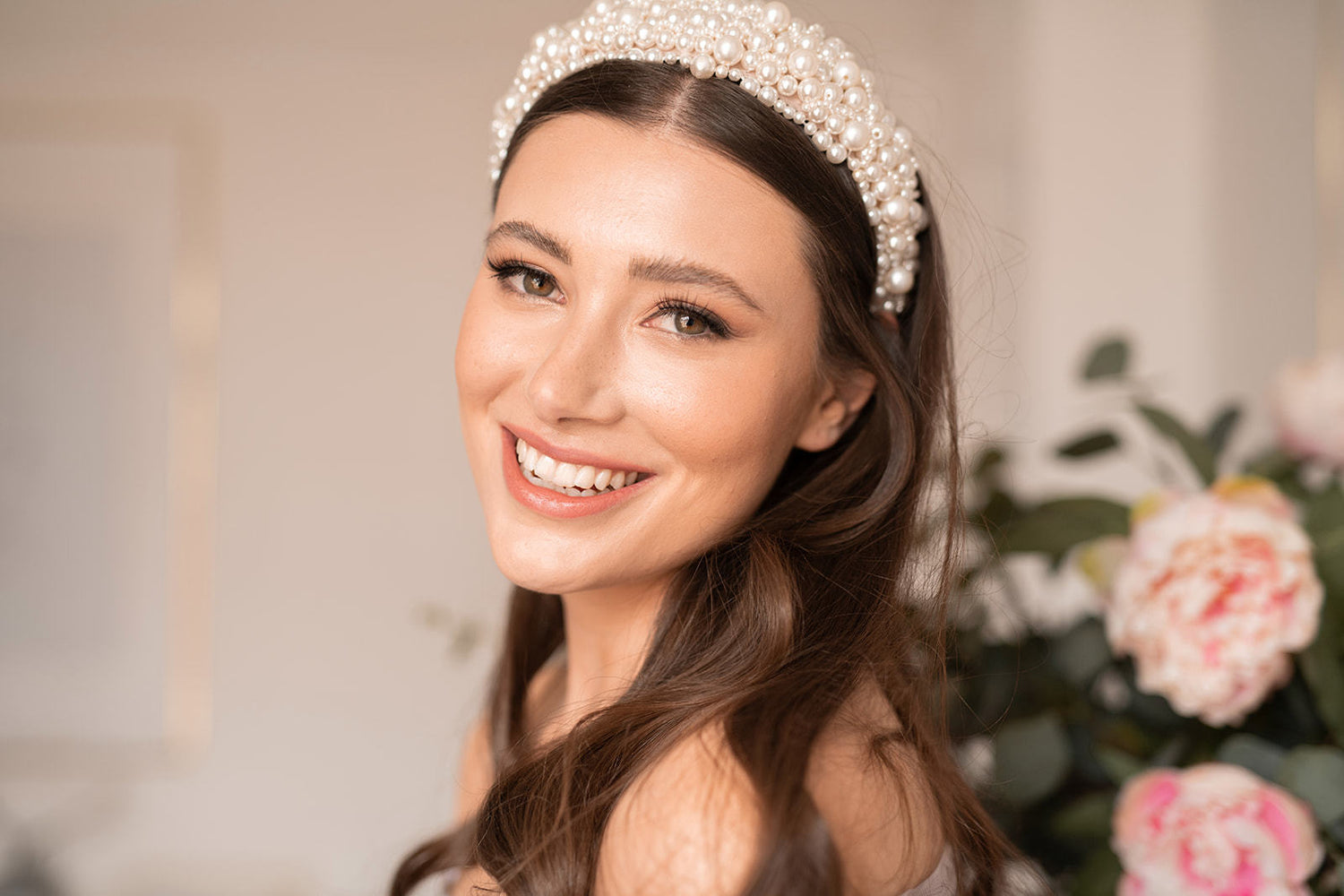 Brunette bridal model smiling while looking down the length while wearing our Devoted Luxe 'Ava' Pearl Headband